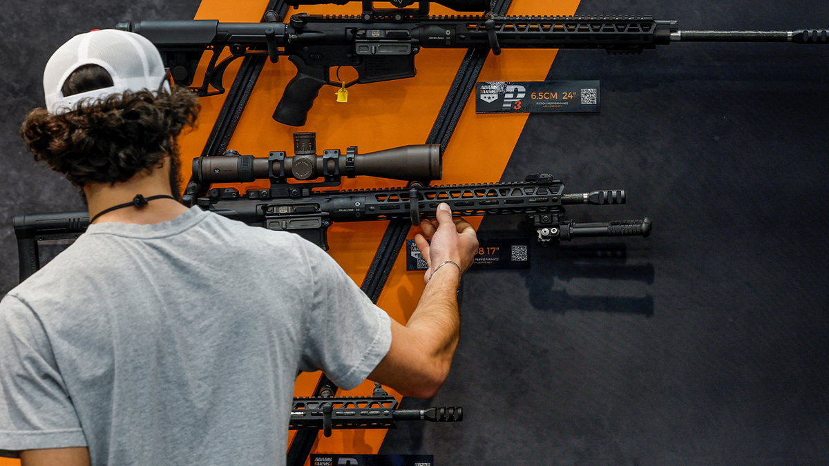 man looks at gun on wall