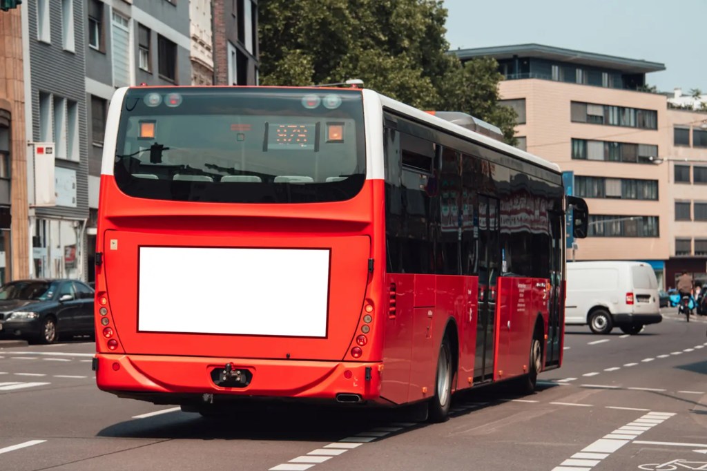 A large red bus in an urban setting driving on the street.