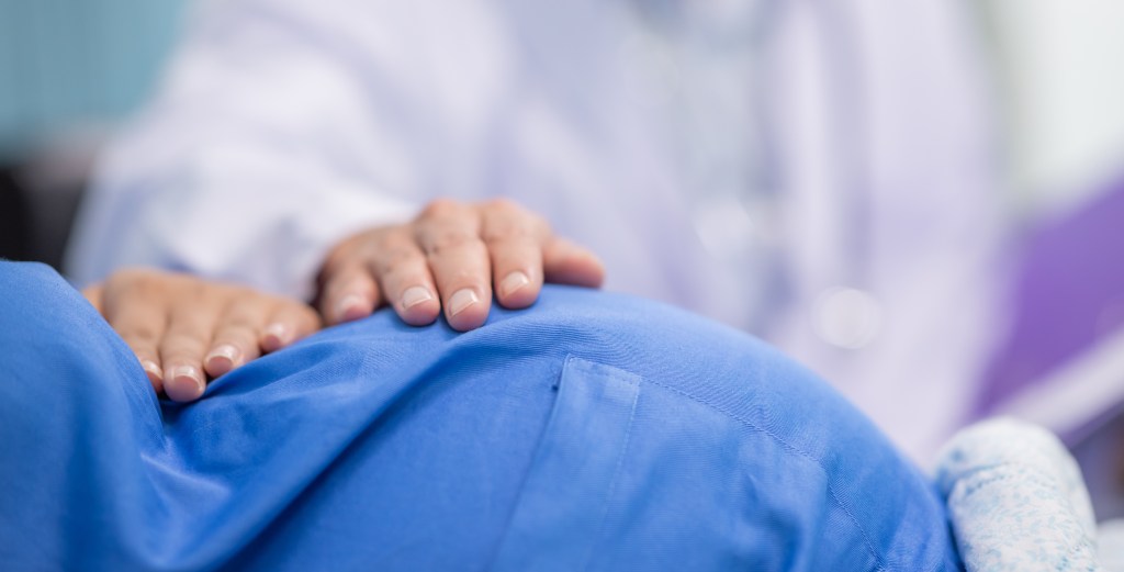 Man male obstetrician doctor in white uniform coat gown with stethoscope to check womb stomach in delivery room.