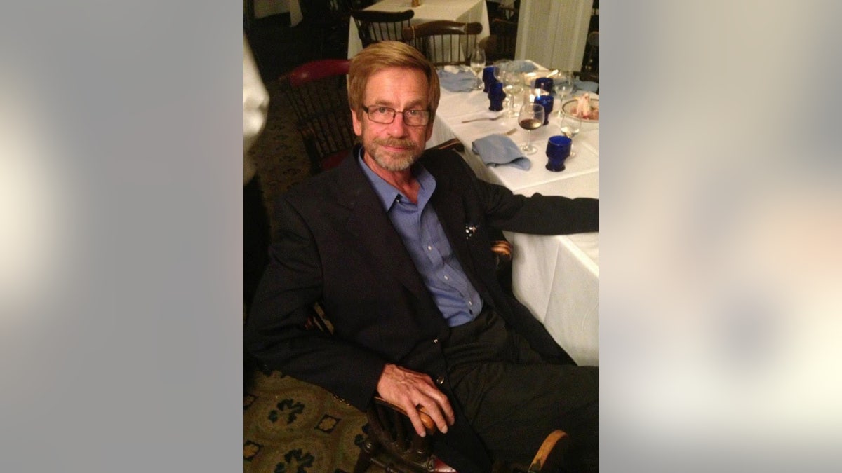 Thomas Randele sitting on a table wearing a black suit and a blue shirt