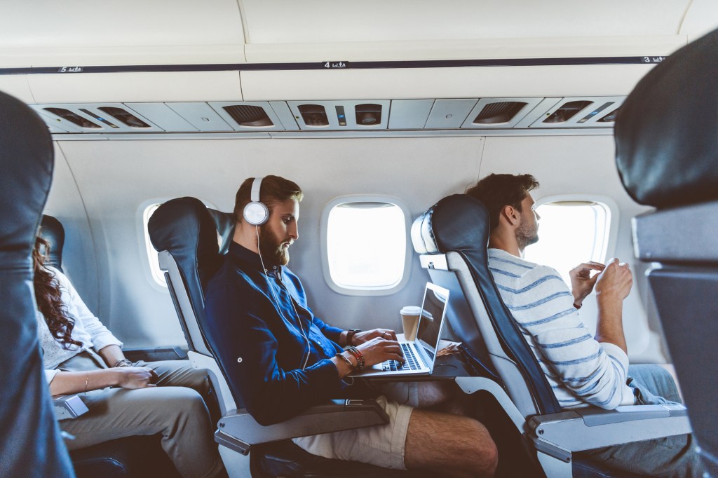 Young bearded man sitting inside an airplane and using a laptop. 