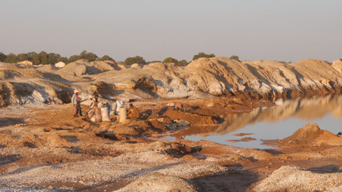 Wide shot view of children sitting and mining for cobalt in Democratic Republic of the Congo, big hills, dark/sandy looking