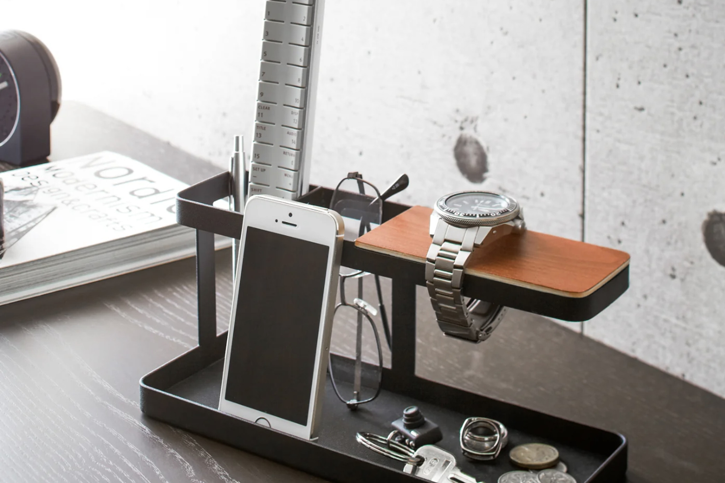 Black and brown two-level desk organizer loaded with small stuff like a phone, a watch, and a pair of glasses.