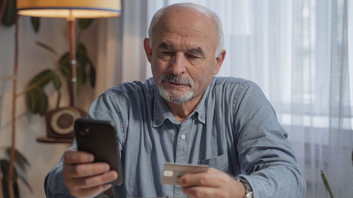 man holding smartphone in one hand, credit card in other