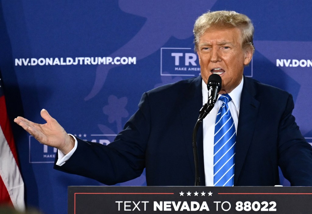 Donald Trump speaking into a microphone at a Commit to Caucus Rally in Las Vegas, Nevada.