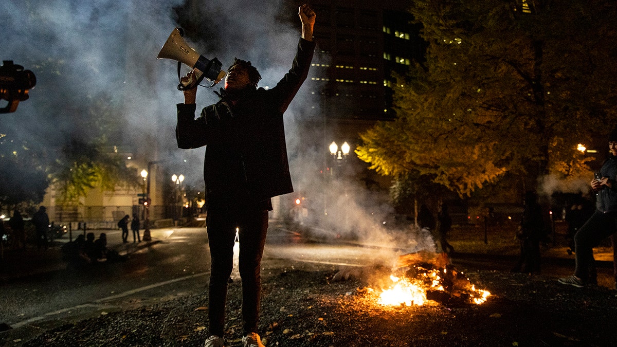 Protester holding microphone chants with small fire burning in middle of the road behind them