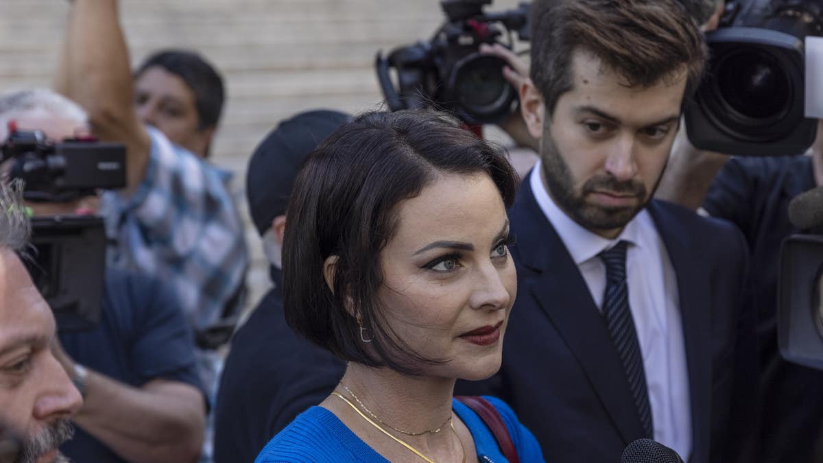 Sarah Ransome in blue dress with short hairspeaks to reporters outside court