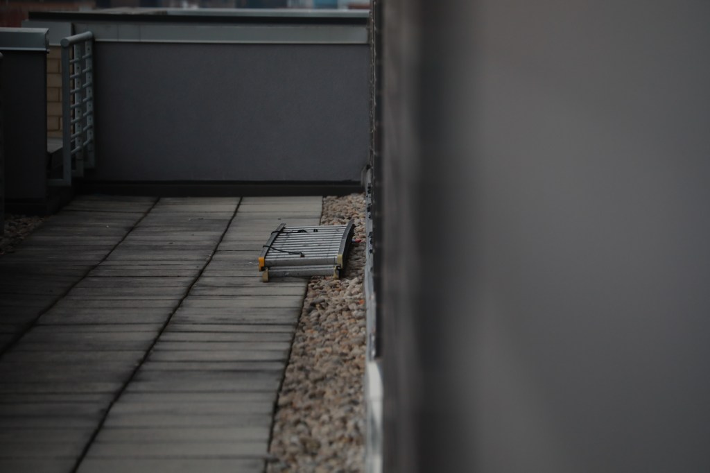 Child has fallen from a high-rise window, landing on a black metal ladder with a shoe possibly of a comic book character.