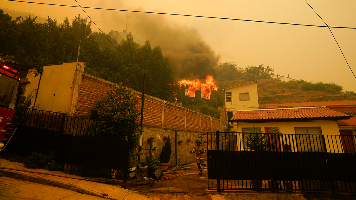 A firefighter runs through a front yard as a building goes up in flames