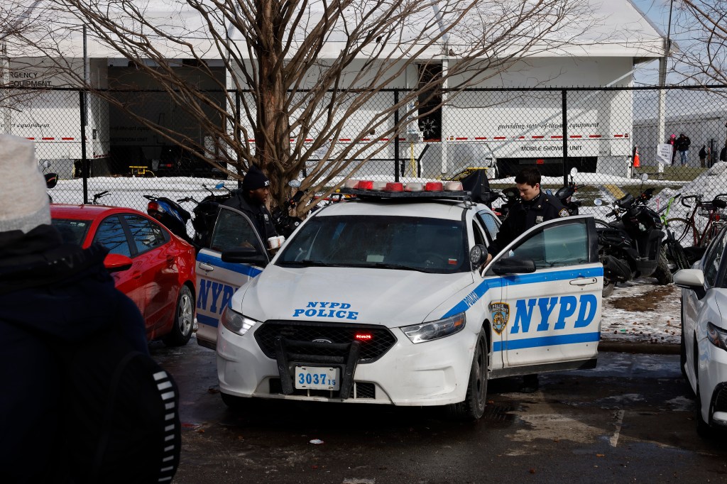 Officer steps into a NYPD car parked on Randall's Island near migrant facility 