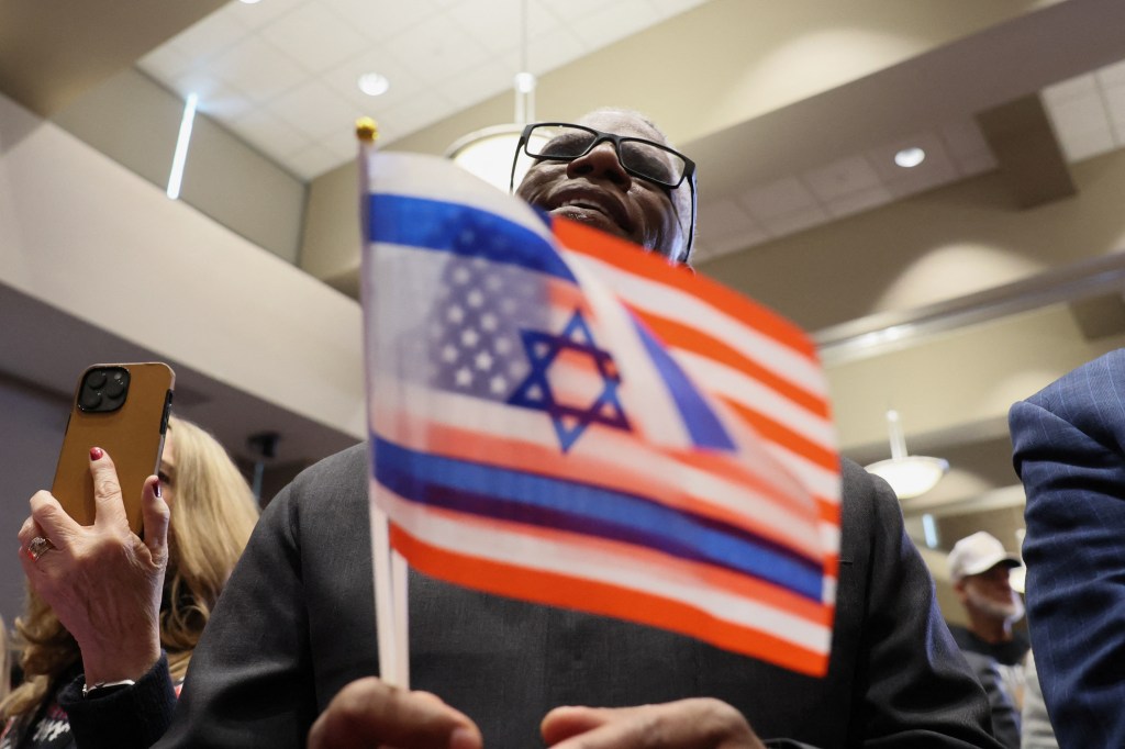 A Trump supporter smiling while holding flags of the U.S. and Israel