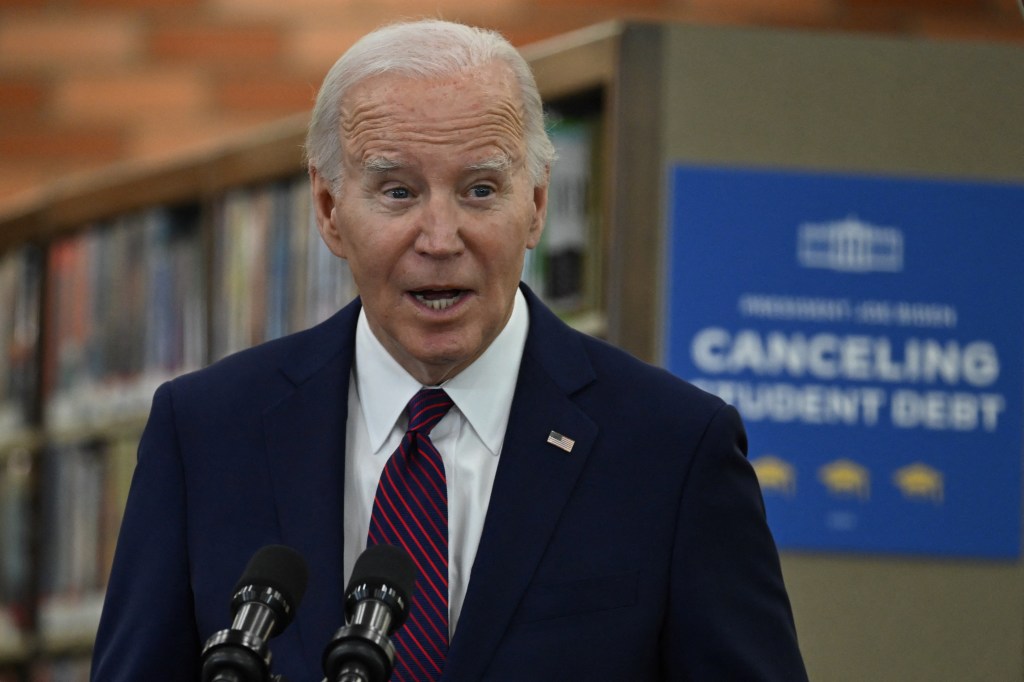 Joe Biden speaking at a podium with microphones in front of him at an event announcing student debt cancellation.