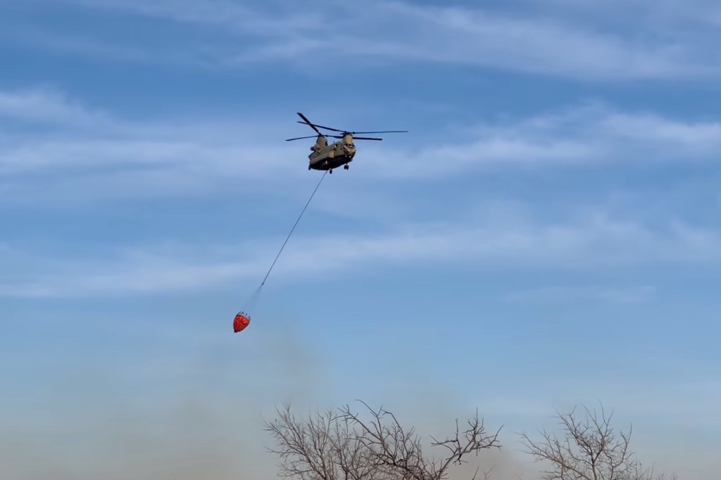 A Texas Army National Guard Chinook helicopter drops water from a bucket on the Smokehouse Creek Fire in the Texas Panhandle.