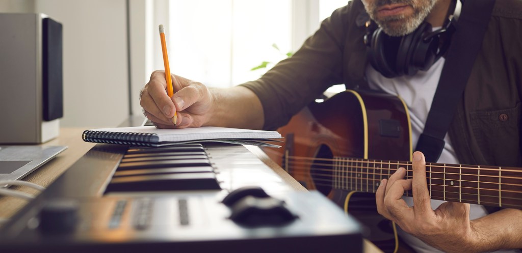 Songwriter passionately writing music in home studio with an electronic keyboard and guitar