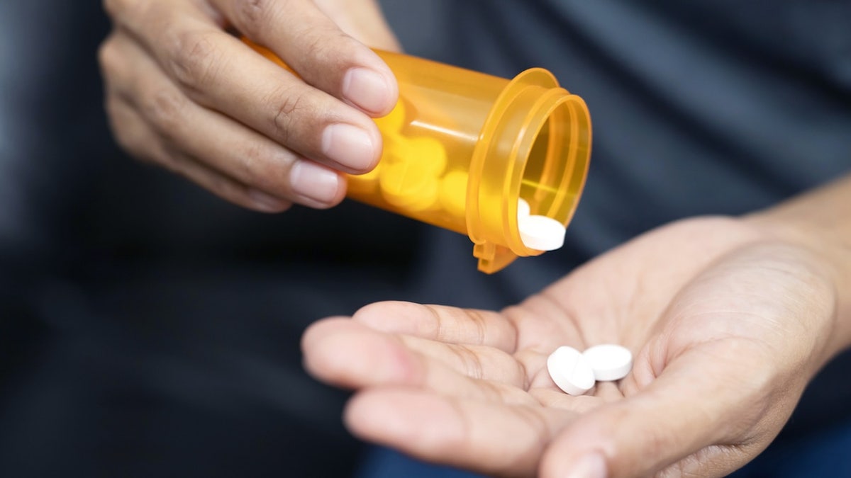 Woman hand with pills on, spilling pills out of bottle on dark background.