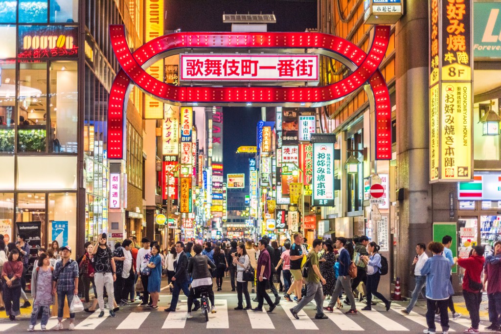A crowd of people walking on a street in Kabukicho district under a large sign